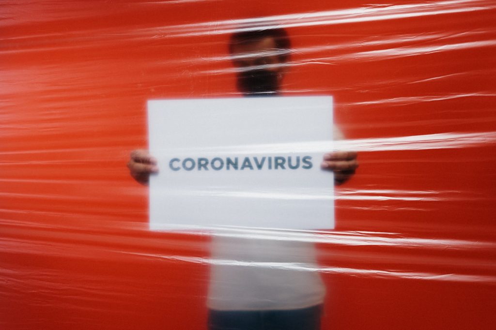 man behind a plastic holding a poster of coronavirus